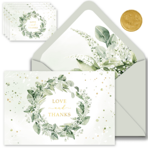 A green floral wreath surrounds elegant wedding thank you cards, conveying gratitude and love in a charming design.