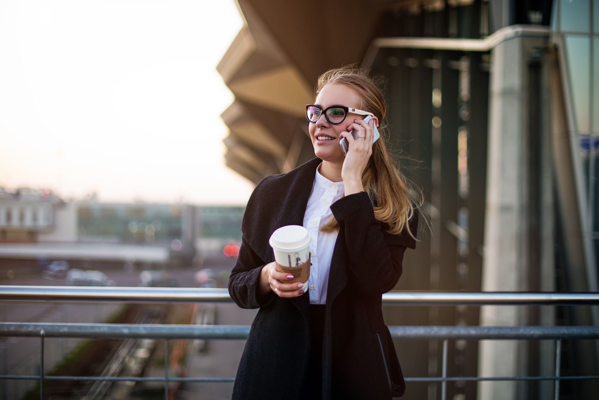 Happy smiling woman successful employee talking via mobile phone while standing with take away coffee outside enterprise during break at job. Female professional owner phoning via cell telephone