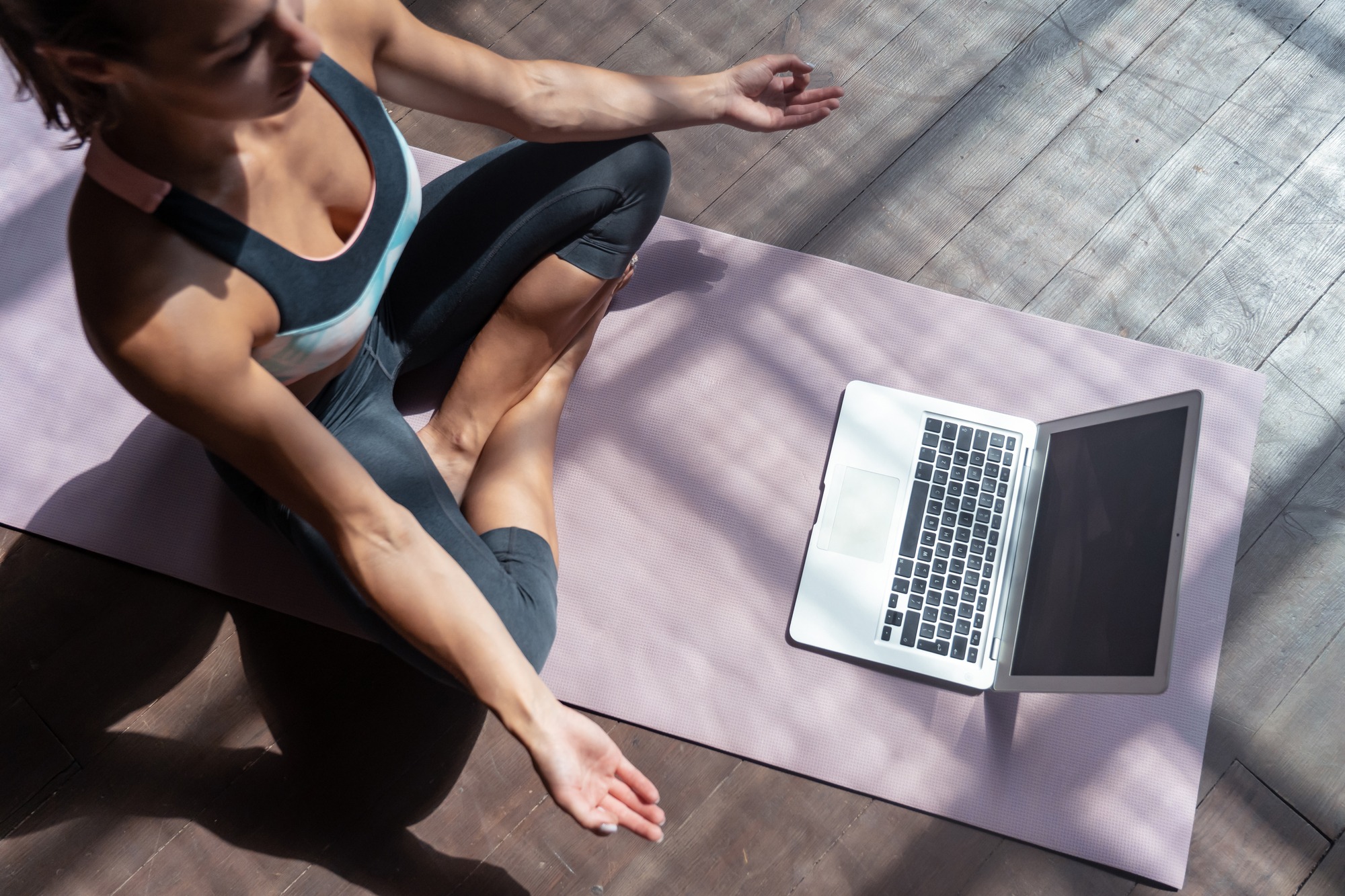 A woman is seated on a yoga mat, engaged with her laptop