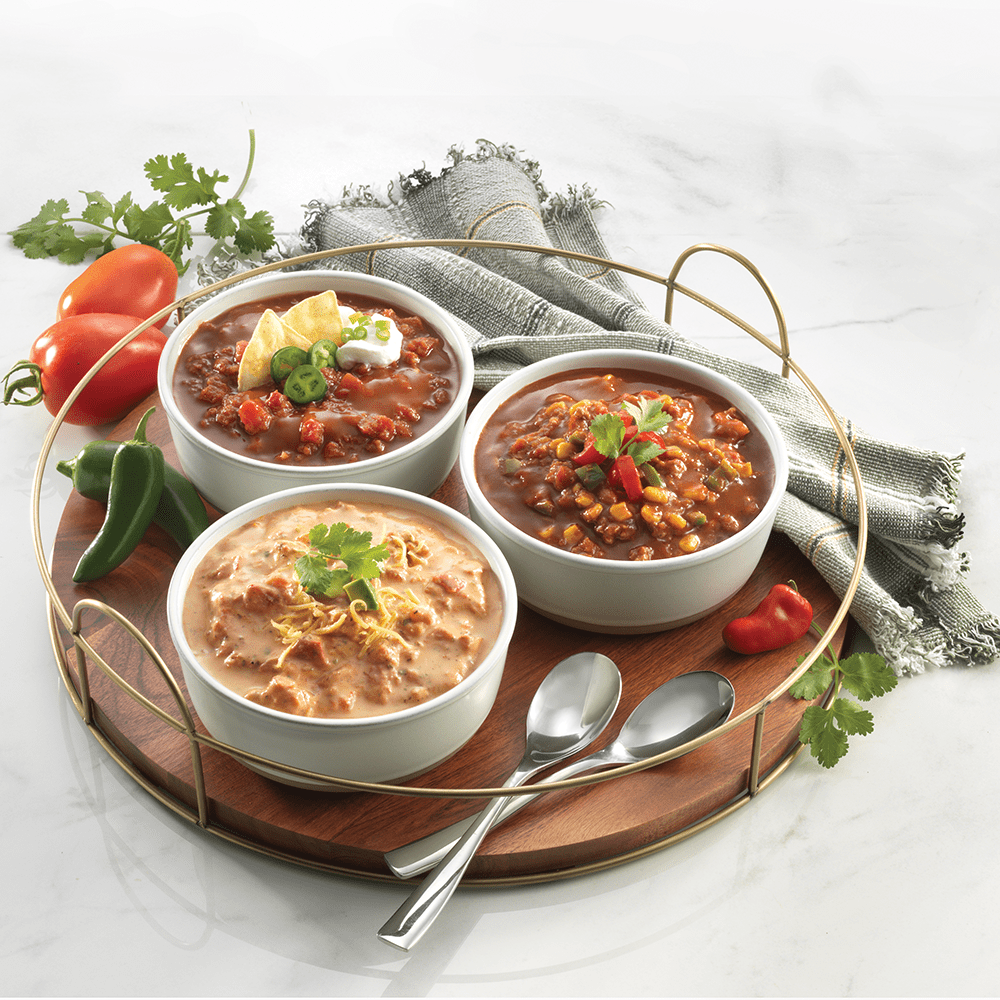 Three bowls of chili and assorted vegetables arranged neatly on a tray