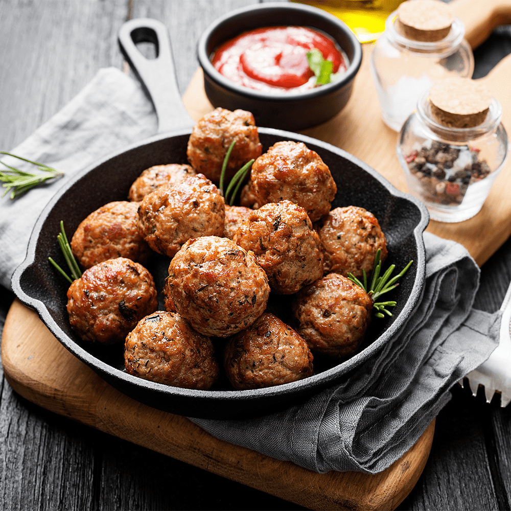 A skillet filled with savory meatballs simmering in rich sauce, garnished with aromatic spices.